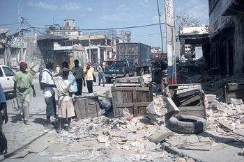 Haitian citizens walking down a debris-strewn street.