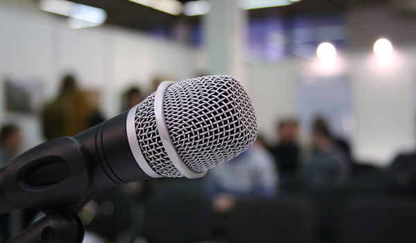 Microphone in foreground with a blurry background of a room with people.