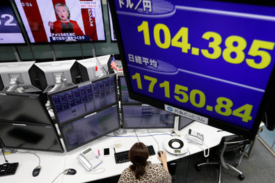An employee of a foreign exchange trading company in Japan working below monitors that displayed the yen’s exchange rate and the American presidential nominee Hillary Clinton.