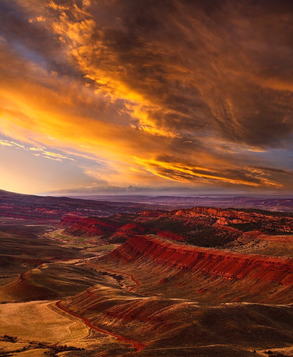 A golden sunset lights the clouds over a landscape of red canyons.