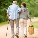Older man with a cane walking with his caregiver from the grocery store