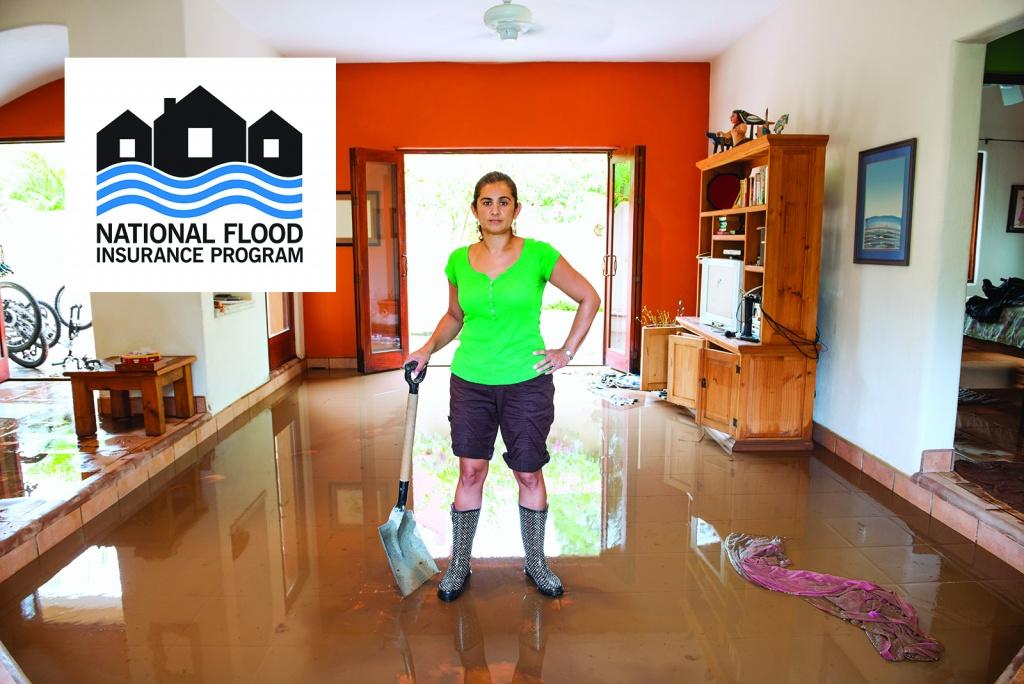 A woman stands in her flooded living room. There are a couple of inches of water over the floor and she has a shovel and water-proof boots on. The National Flood Insurance Program logo has been embedded into the top left corner of the photo.