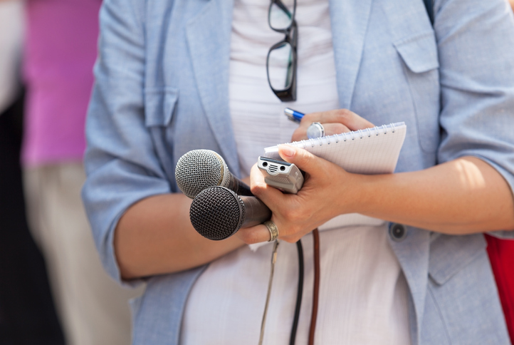 Reporter is holding microphones, tape-recorder and notepad