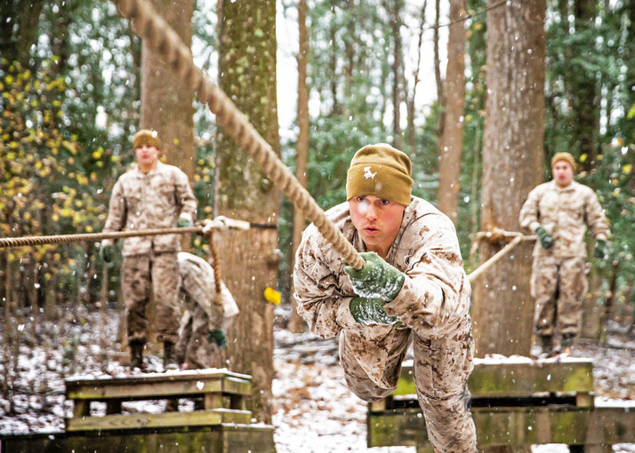 A Marine climbs an obstacle rope while two others watch.