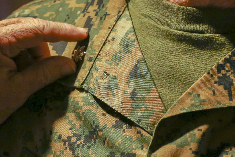 A hand reaches in to remove the rank insignia from a green Marine Corps uniform.