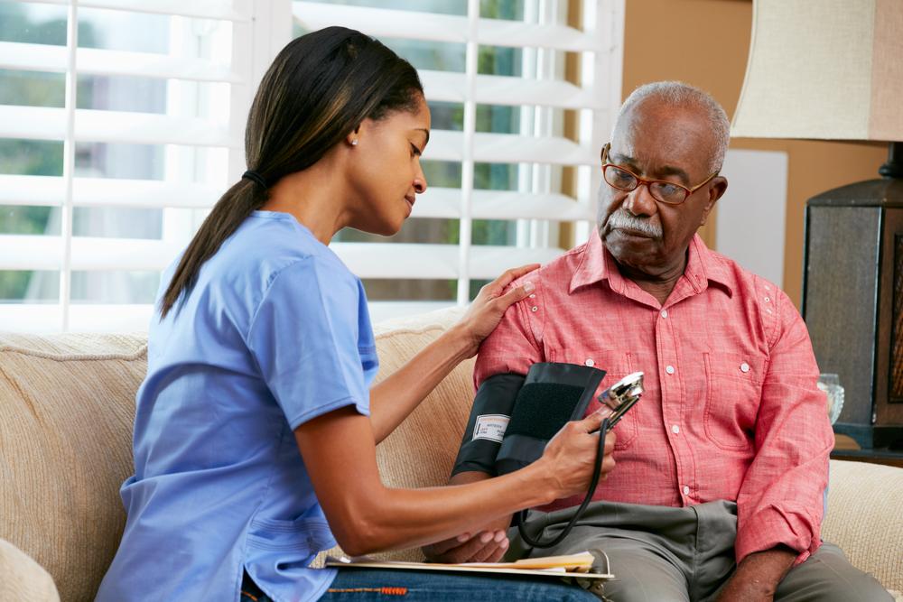 Health professional adminstering a blood pressure reading with a patient in a chair.