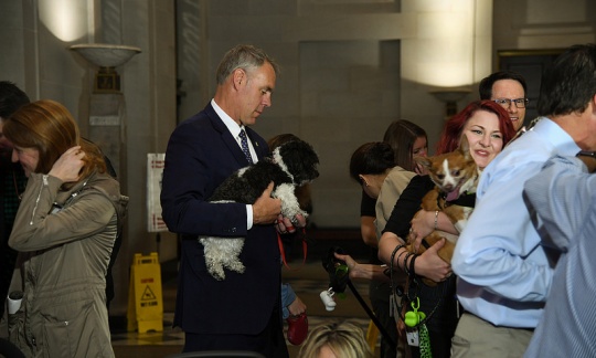 Secretary Zinke holds his small dog in his arms surrounded by other men and women