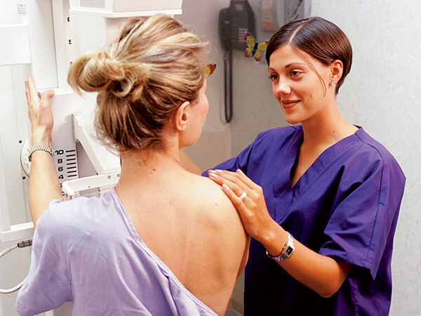 A woman talking with a female technician while getting a mammogram