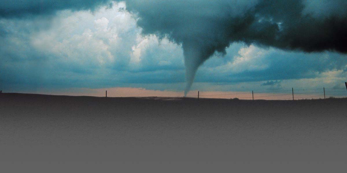 Photo of a tornado in an open landscape at late afternoon.