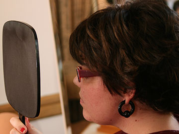 Una mujer se prueba una peluca frente a un espejo de mano.