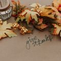 ribbon-like arrangement of fall leaves on a table with a votive candle and Give Thanks handwritten in script
