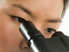 An Asian woman looks into a microscope.