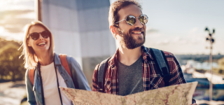 Photo of two tourists wearing sunglasses and smiling while holding a map