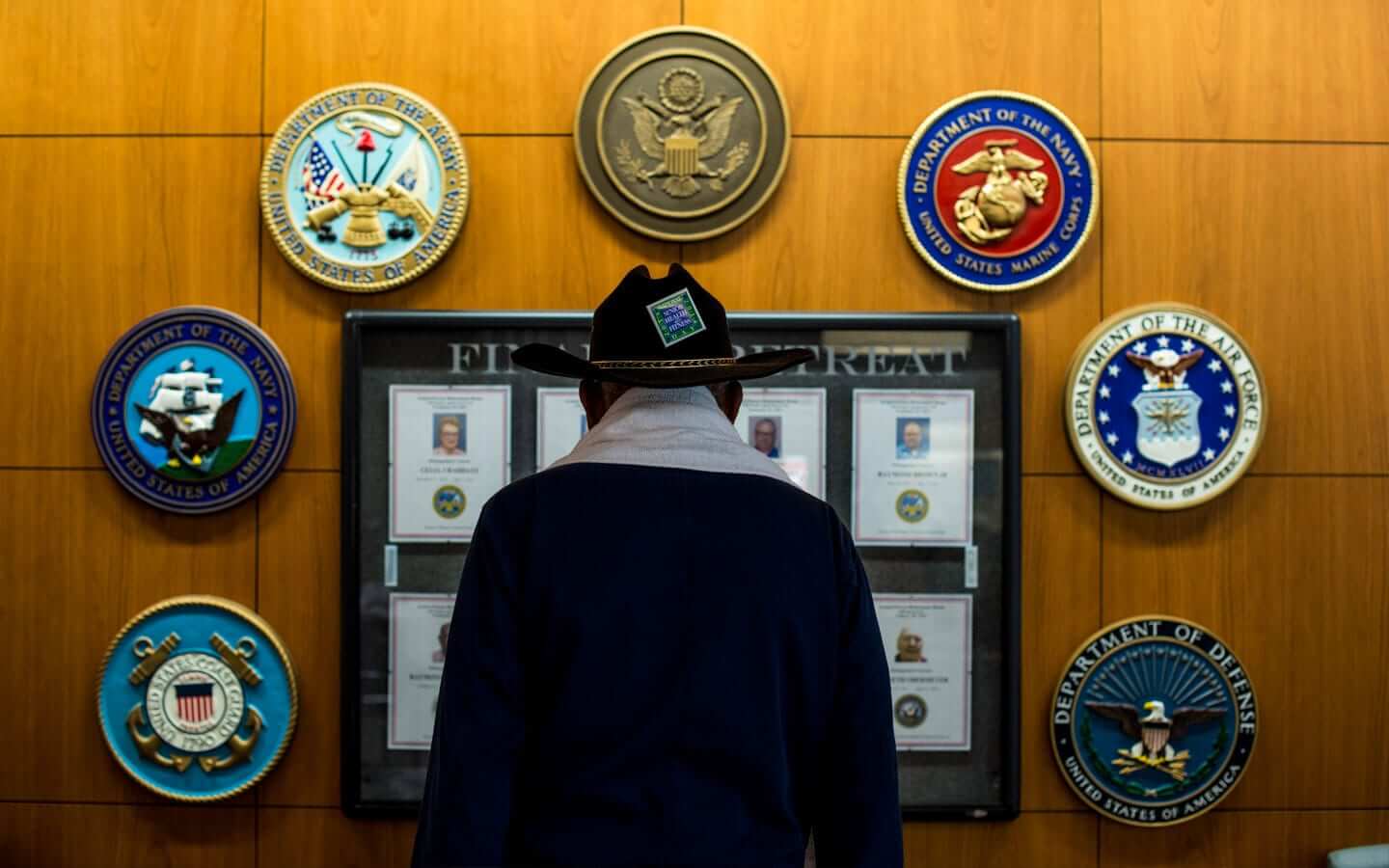 An old male Veteran is facing a wall with symbols/icons of military branches.