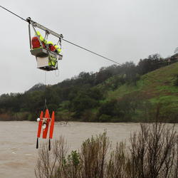 Two technicians in a cablecar over a river, with an instrument hanging below them