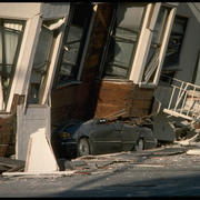 Photo shows the major collapse of a building following an earthquake, the building has fallen onto and crushed a car completely.