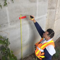 Image shows a USGS scientist in a PFD taking a high-water mark