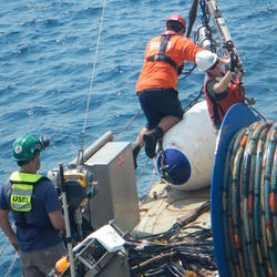Image shows USGS scientists in PFDs collecting a seismic airgun while at sea