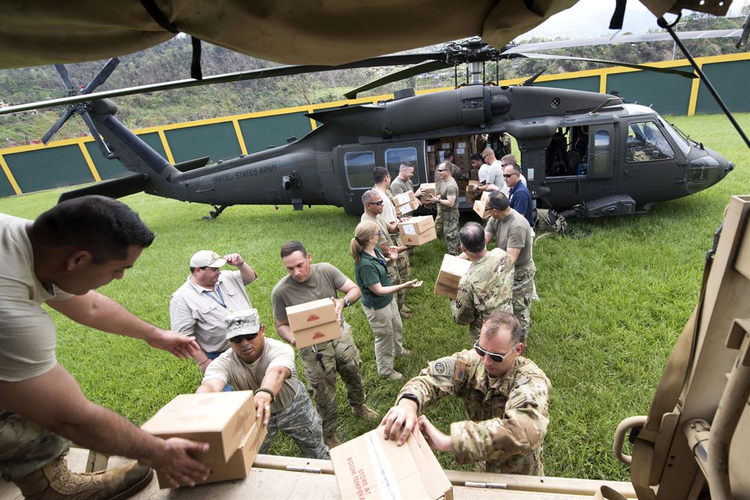 Two lines of people unload boxes from a helicopter.