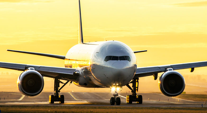 Front view of airplane on tarmac with yellow sunset behind it