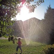 Boy running on lawn under water sprinkler