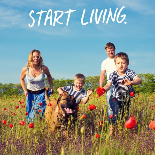 Young woman and man with two little boys holding hands. All are running towards the camera in a meadow with flowers with their dog, smiling. Text over blue sky reads, "Start living."