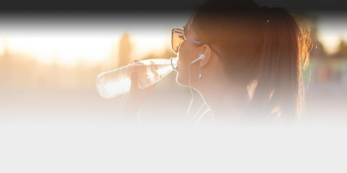 Close up picture of woman drinking water with sun behind her.