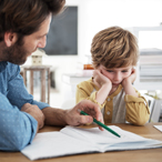 Stock image of an adult male points to a notebook page and a child looks on, discouraged, with head in hands.