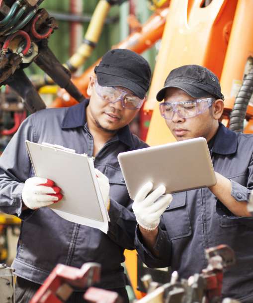 A pair of manufacturing technicians compare notes on a clipboard and a tablet. 