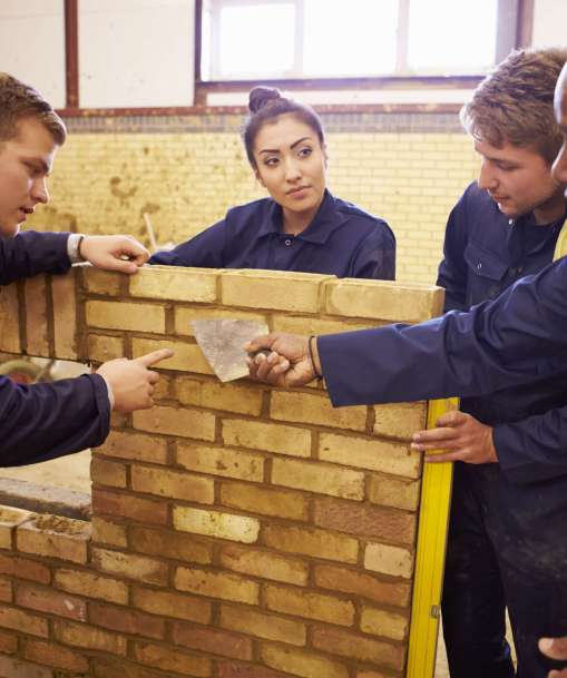 A Bricklaying instructor teaches a group of students the tricks of the trade