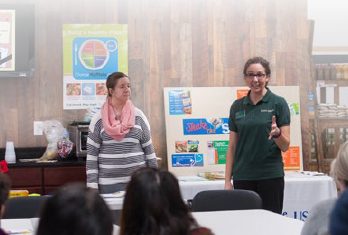 two adults speaking to a group with the MyPlate poster in the background