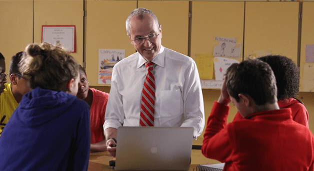Photo: Phil Murphy behind a laptop talking to kids