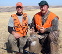 Photo of two hunters wearing hunter orange with recently harvested deer. Rifle with scope in the foreground.