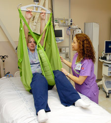 A health care provider is using a ceiling lift to safely move a woman out of her hospital bed
