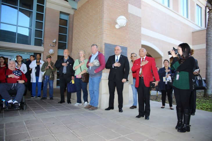 (At right) Valley Morning Star reporter Alana Hernandez takes photos while VA employees, and guests place their right hands over the left side of their chest (where the heart is located) in order to take part in reciting the pledge of allegiance to the flag of the United States of America during a special event held in observance of National Native American Heritage Month, which took place at the VA outpatient clinic in Harlingen, Texas, on November 16, 2018. At one point in time there were approximately 100 people gathered in and around the entrance to watch the performances by the Lipan Apache tribe of Texas. (U.S. Department of Veterans Affairs photo by Luis H. Loza Gutierrez) 