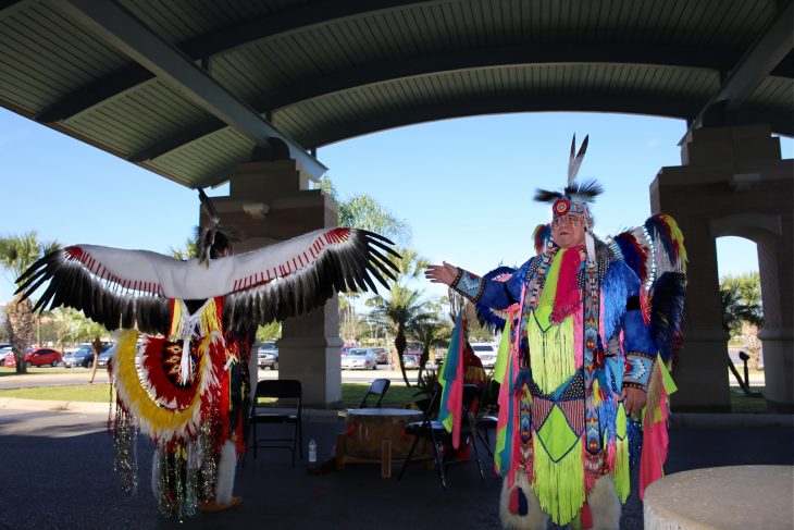 Robert Soto, the vice chairman of the Lipan Apache Tribe of Texas, explains the history and significance of the eagle feathers worn by a tribal member preparing to perform the Eagle Dance during a special event in observance of National Native American Heritage Month, which took place at the VA outpatient clinic in Harlingen, Texas, on November 16, 2018. (U.S. Department of Veterans Affairs photo by Luis H. Loza Gutierrez)