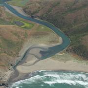 View from the sky looking at mouth of river with lots of sediment deposited at a beach.