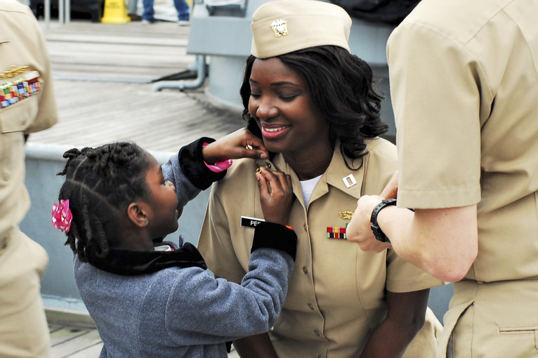 A girl affixes pins to a smiling sailor's uniform.