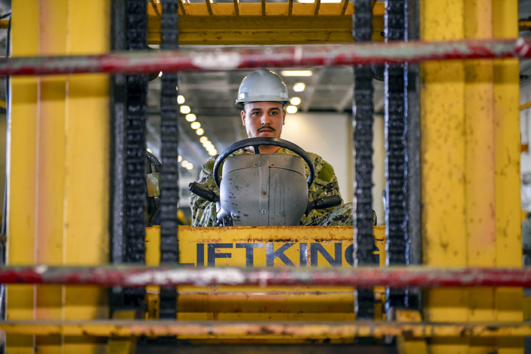 A sailor operates a forklift on a navy ship.