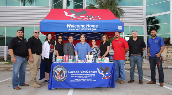 Eleven people standing at a table in front of a Vet Center