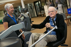 Older man exercising while trainer looks on. 