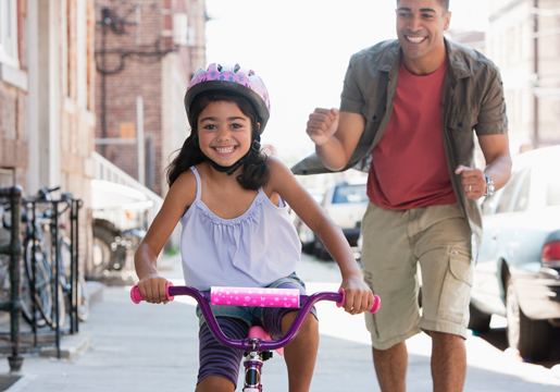 Girl riding bike with father cheering