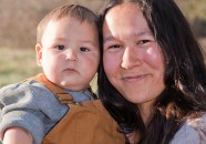 A smiling Native American woman standing outside holding her baby