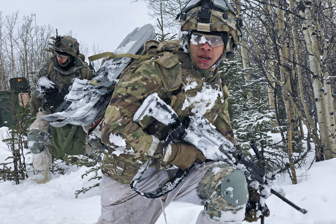 A soldier walks through the snow with a rifle.