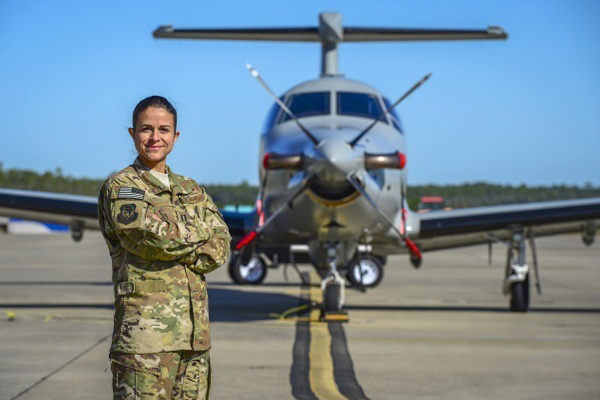 An airman poses next to a plane.