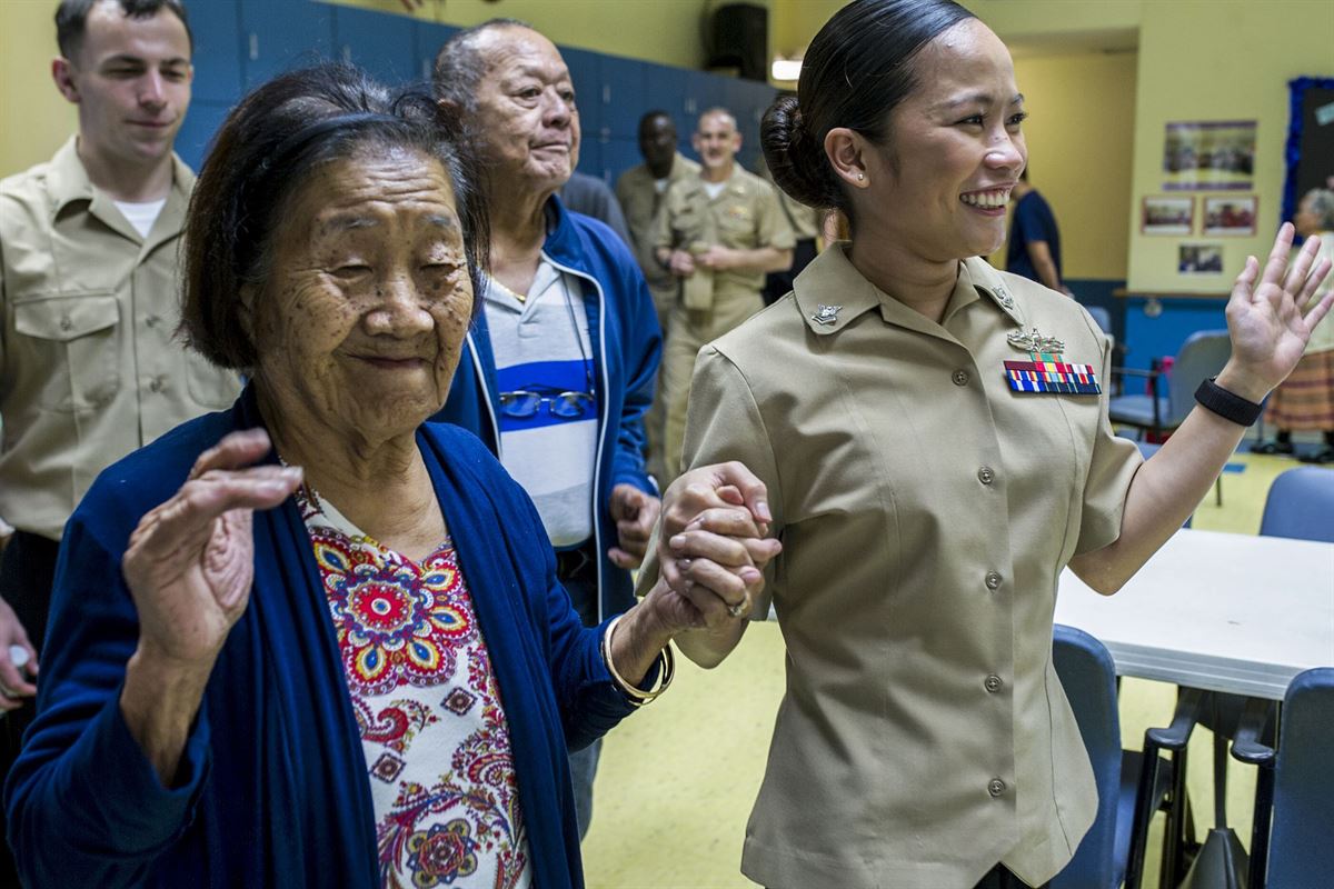 A sailor holds hands with an elderly woman, as they both smile and raise their hands.