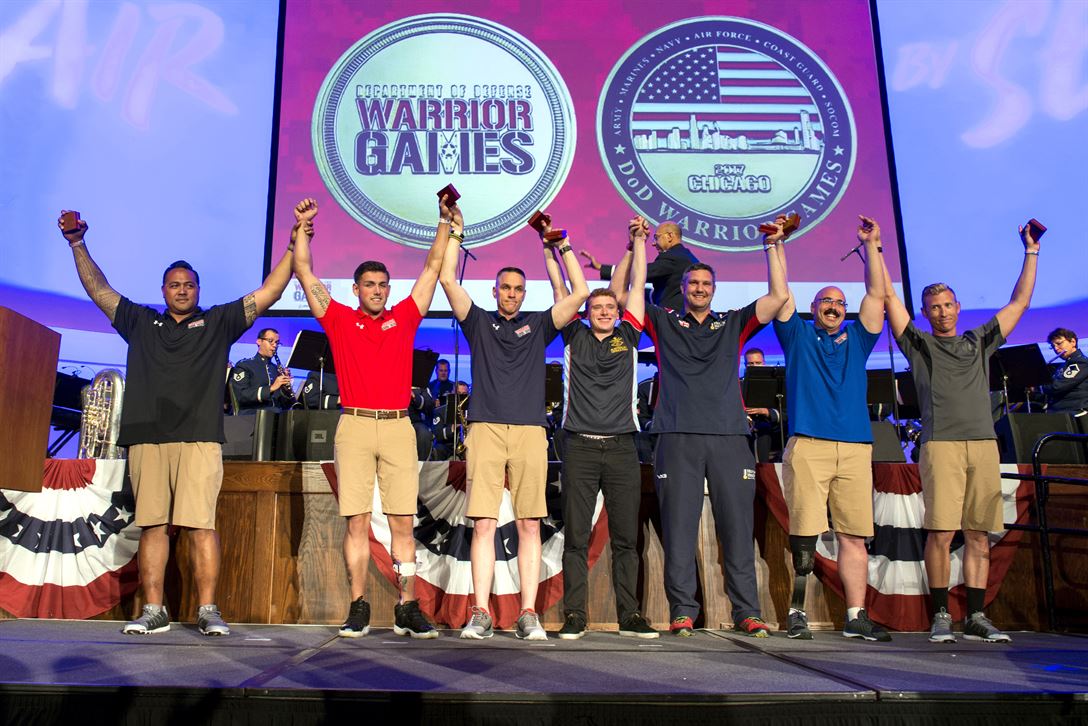 Team representatives raise each other's arms on stage during a ceremony.