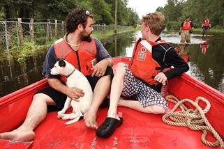 People and a dog sit in a boat, while members of the Coast Guard walk behind it in knee deep water.