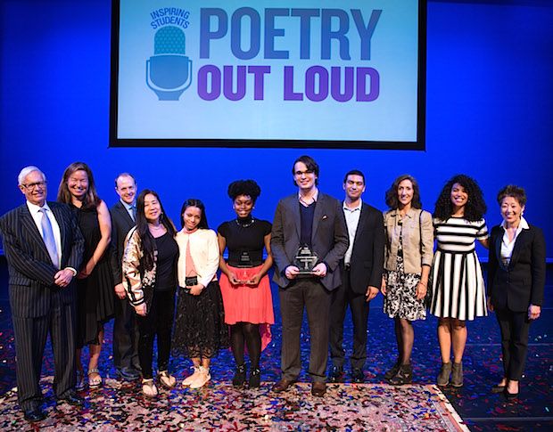 A group of men and women stand in a line on stage with a Poetry Out Loud sign behind them.