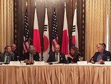 A group of people sitting at a table in front of the flags of the United States, Japan, and Korea